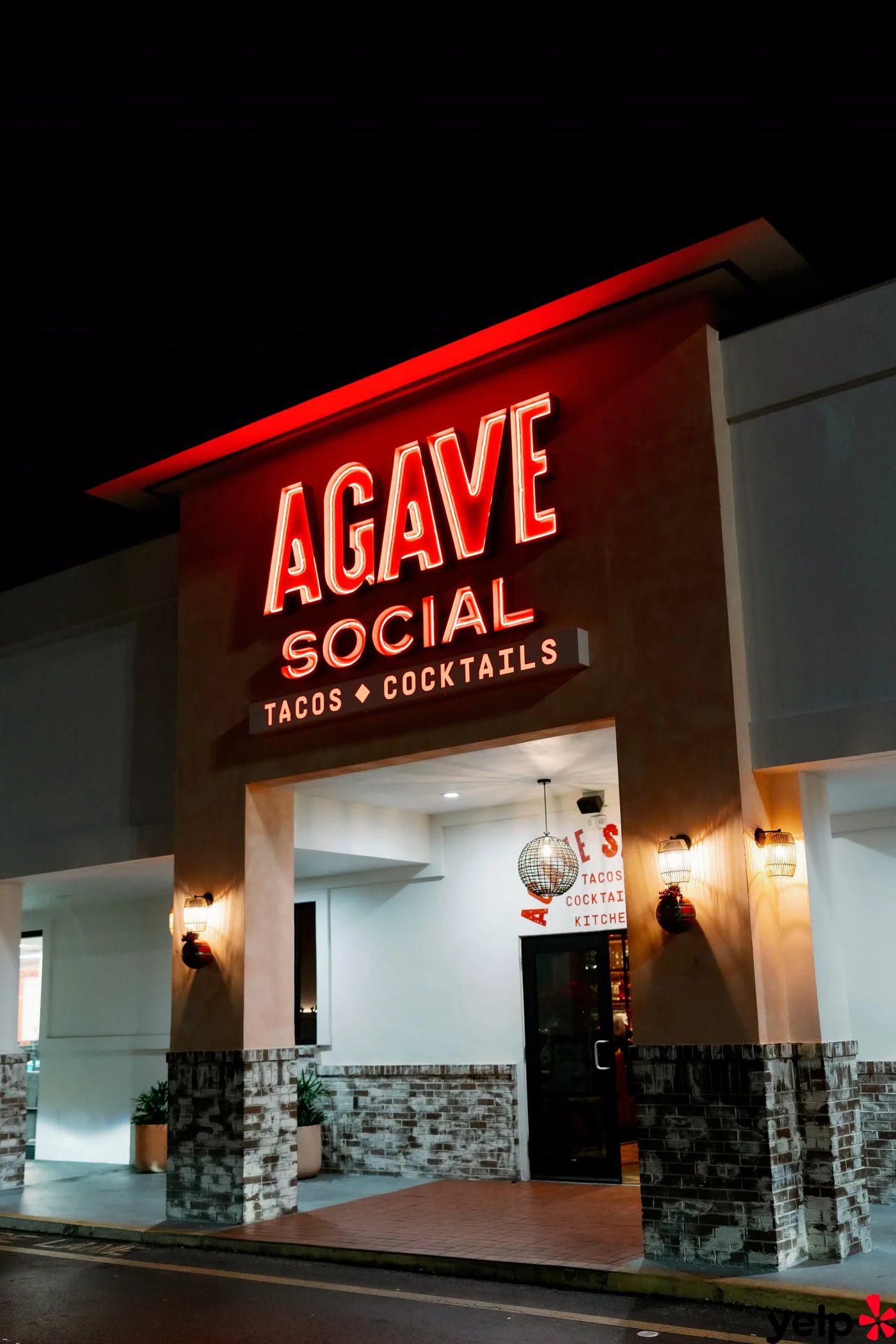 The red neon Agave Social — Tacos · Cocktails sign above the entrance at night